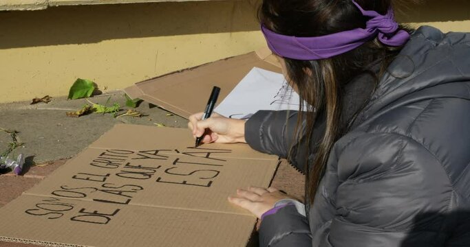 young woman preparing poster on the ground for feminist protest in Spanish