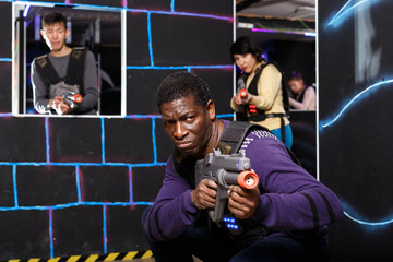 Portrait of emotional African American man aiming laser gun at other players during lasertag game in dark room