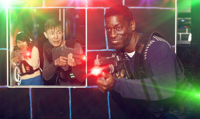 Emotional African man with his laser pistol playing laser tag with friends at a dark labyrinth