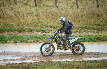 Obraz premium motorcyclist ridiing his motorbike across a water-logged muddy track 