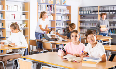 Obraz premium Schoolchildren doing their homework in the school library write out a synopsis from the textbook in a exercise book