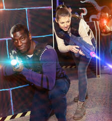 Portrait of cheerful multiracial couple with laser guns having fun on dark lasertag arena