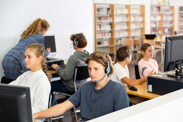 Fototapeta premium Group of young girls and boys sitting in computer classroom of library and exercising.