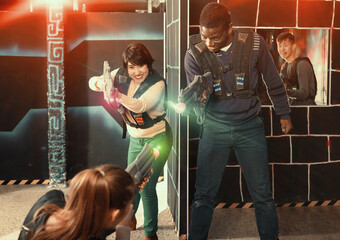 Modern friendly people of different nationalities with laser pistols playing laser tag on dark labyrinth