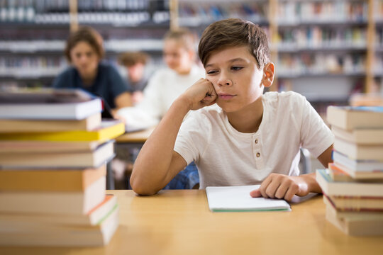 Bored teenage boy trying to prepare for exam in school library