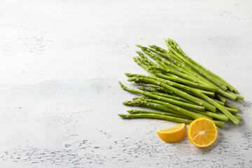 Fresh young asparagus with lemon on light gray background