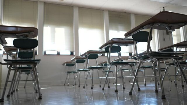 Desks in empty dark high, middle, or elementary school classroom with light coming through windows.