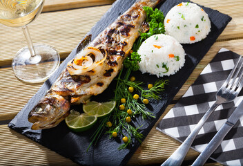 Image of deliciously baked whole trout with rice, served with lemon and greens