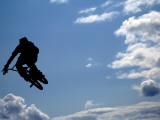 Naklejka na ściany i meble BMX rider performing air trick clouds as background
