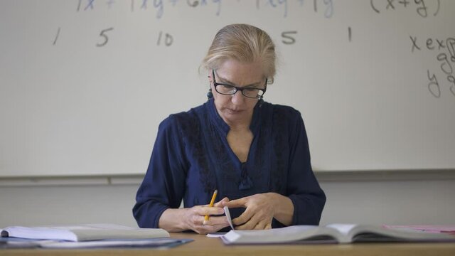 Portrait of frustrated tired high school math teacher sitting on desk talking to students.