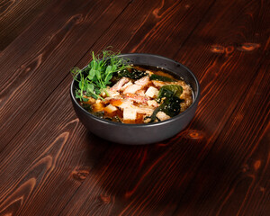 Food, soup with noodles, chicken, tofu cheese, seaweed, sesame seeds in a plate on a dark wood background