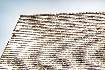 A shingled roof in winter offering an imperfect grid of snow filled horizontal shingles.