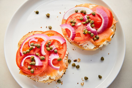 Top View of Lox, Tomatoes, Capers, Red Onion, and Cream Cheese on Bagel on White Plate - Powered by Adobe
