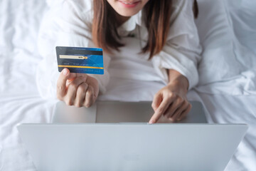 woman using computer laptop and credit card for online shopping while making order on bed in morning at home. technology, ecommerce, digital banking online payment and apartment living concept