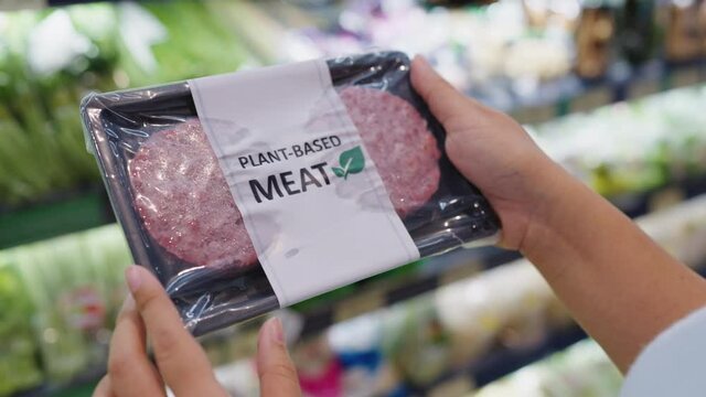 Close-up hand carry choose zero pork soy bean faux peas cutlet gluten free read beyond non-meat lab label. Buy raw fake beef tray in asia store veggie burger patty for health care eat diet meal cook.