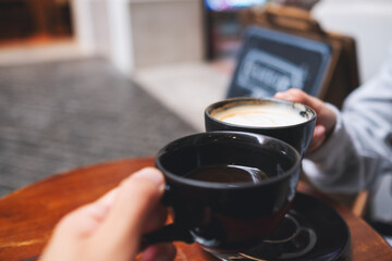 Closeup image of a man and a woman clinking coffee cups together in cafe