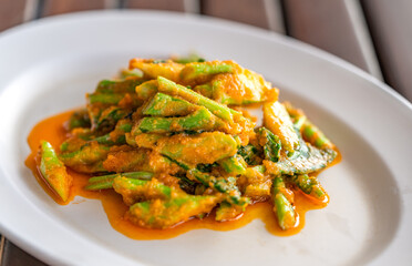 Stir fried Kale or Chinese broccoli with salty egg in white plate on wooden table, close up Thai food image of Chinese broccoli with salty egg, natural light.