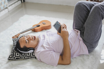 Young asian man relaxing, lying down, singing happily in apartment