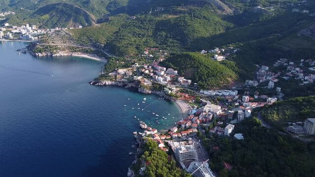 Bird's eye view of holiday town by the sea. Town is located at the foot of the mountain with green forests.
