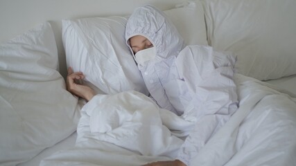 Sleepy tired exhausted lady in white protective biohazard suit with face mask tacking a nap during...