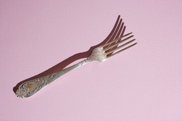 Old vintage fork on pink background with hard shadows.