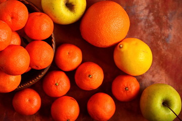 Heap of tangerines in wooden bowl and scattered around fruits, lemons, green apples, oranges and tangerines on brown background. Top view, flat lay
