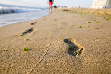 Shallow depth of field (selective focus) details with footprints in the beach sand on a calm and warm summer day at the Black Sea in the Obzor resort in Bulgaria.