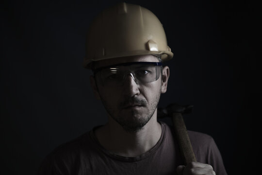 Miner face on black background.Head tired miner in helmet and glasses.He holds a hammer on his shoulders.