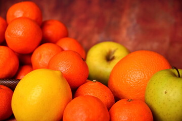 Scattered fruits, lemons, green apples, oranges, tangerines close up on blurred background of heap of tangerines. Selective focus