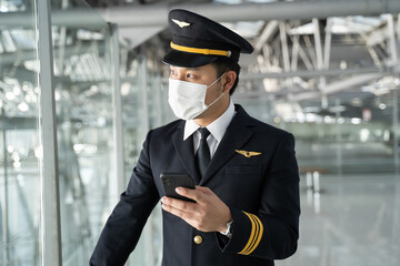 Asian Airliner pilot wearing face mask, standing in airport terminal.  © Kawee