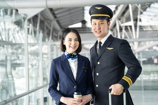 Asian airliner pilot and air hostess walk together in airport terminal
