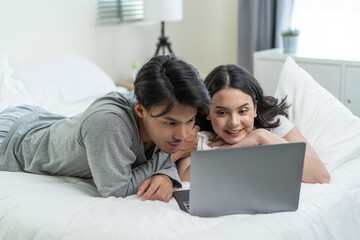 Asian attractive happy young couple watching movie on bed in bedroom. 