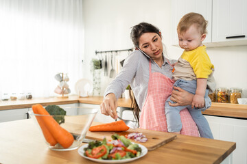 Caucasian busy mother doing housework with baby boy toddler in kitchen