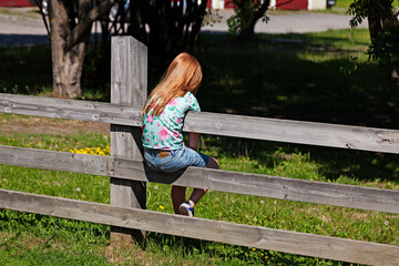 Umea, Norrland Sweden - June 24, 2020: little girl with red hair sits on a fence and is bored