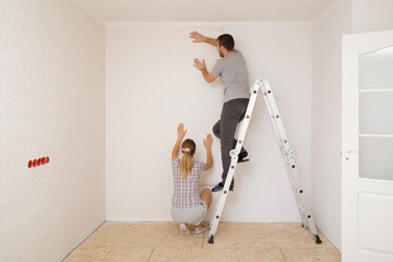 Young adult couple making interior change. Man standing on metal ladder and woman help applying new...