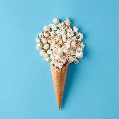 Ice cream cone with spilled popcorn on pastel blue background.