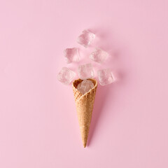 Ice cream waffle cone with ice cubes on pink background. Minimal cold summer food concept.