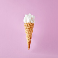 Sugar cubes on ice cream cone on pink background. Sweet food addiction and sugar diet for health