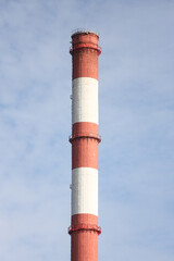 Tall, thin Two Color red and white chimney on the background of blue sky with clouds.