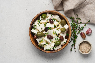 Soft feta cheese with olive oil, herbs and olives in wooden bowl on white background. Pieces of marinated cheese with fresh thyme
