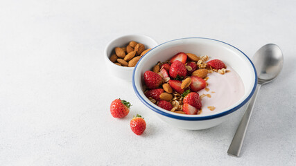 Strawberry yogurt with fresh berries, homemade granola, almonds in bowl. Healthy breakfast on light background