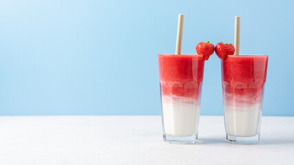 Protein rich smoothies with yogurt and frozen strawberries in glass on light blue background. Concept of drinks for lovers on Valentine's Day. Bright berry as a symbol of the heart