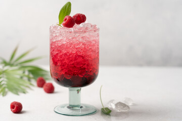 Glass of bright pink raspberry drink with crushed ice on light background. Refreshing berry summer drink
