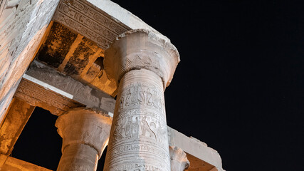 Ancient Egyptian columns against a dark night sky with stars. Carvings, hieroglyphs are visible....