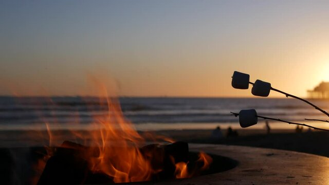 Campfire pit by Oceanside pier, California USA. Camp fire on ocean beach, bonfire flame in cement ring place for bbq, sea water waves. Heating, roast or toast marshmallow on stick. Romantic sunset sky