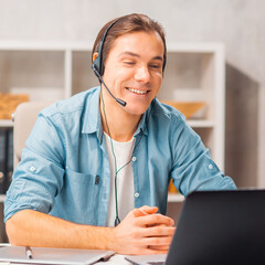 Young man in a headset works at a laptop computer. Freelancer, remote worker or student workplace....