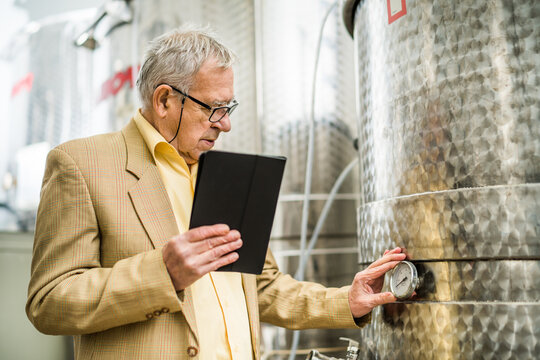 Portrait of senior man who owns winery. He is standing beside wine storage tanks and examining cooling process. - Powered by Adobe