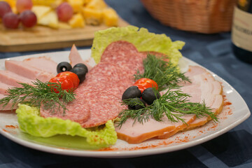 Cold cuts smoked sausage and bacon with green salad leaves, olives and tomatoes, served on a white plate.