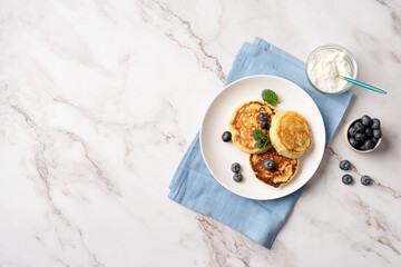 Cottage cheese pancakes served with curd and blueberries, top view flat lay on marble background, copy space