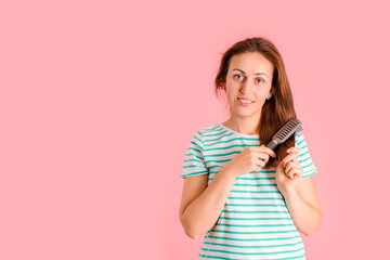A beautiful middle-aged brunette with a smile and a calm look does her hair with a massage comb on a pink background
